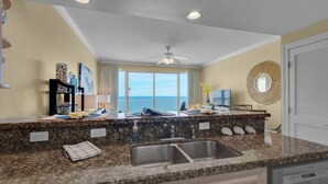 A modern kitchen with granite countertops, a double sink, and a view of the ocean. - Boardwalk Beach Resort Unit 905 (Panama City Beach)