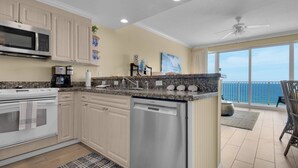 A modern kitchen with a Bosch dishwasher, a microwave, and a stove. There is a balcony with a view of the ocean. - Boardwalk Beach Resort Unit 905 (Panama City Beach)