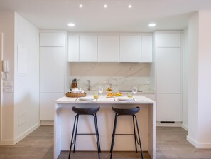 A modern kitchen with white cabinets, a marble backsplash, and a central island with stools. - Apartment in Andalucía del Mar for 4 persons | ADM 5-316 (Puerto Banús - Marbella)