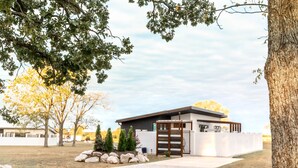 A modern building with a gated entrance, surrounded by trees and a gravel path. - Private modern luxury vacation rental (Stockton)