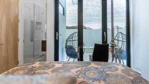 A bedroom with a bed, a wardrobe, and a sliding glass door leading to a balcony with a table and chairs. - Private modern luxury vacation rental (Stockton)