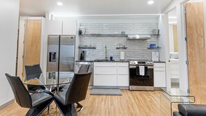 A modern kitchen with white cabinets, stainless steel appliances, and a glass dining table with chairs. - Private modern luxury vacation rental (Stockton)