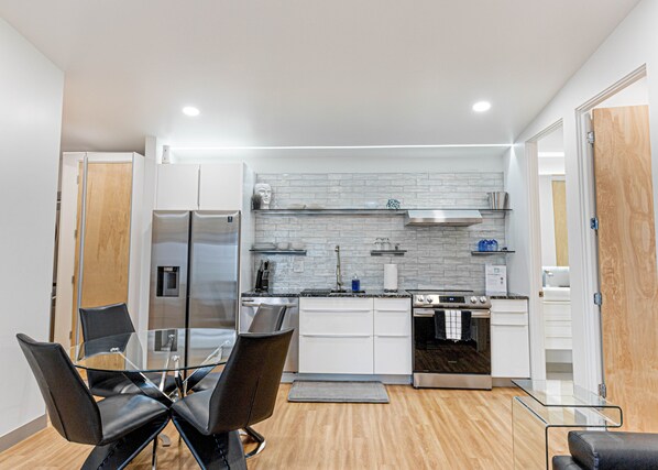 A modern kitchen with white cabinets, stainless steel appliances, and a glass dining table with chairs.