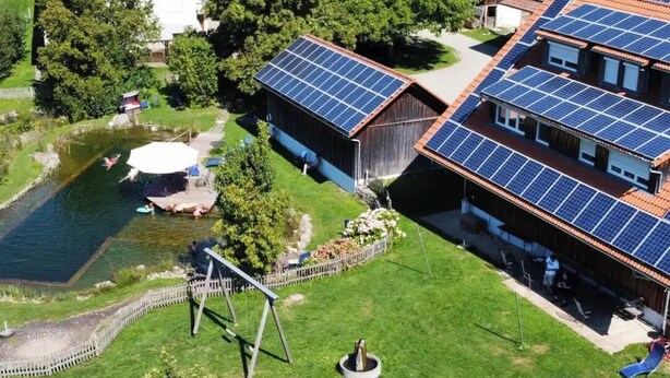 Ett bostadsområde med flera hus, där varje hus är utrustat med solpaneler. Det finns en swimmingpool och en gunga på gården.