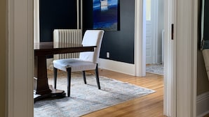 A room with a wooden floor, a white chair, a table, and a painting on the wall. - Victorian Home near downtown, Georgian Bay and many bike & hiking trails (Collingwood)