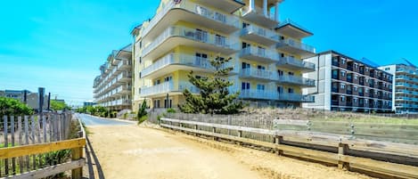 A multi-story hotel with balconies, located near a sandy beach area.