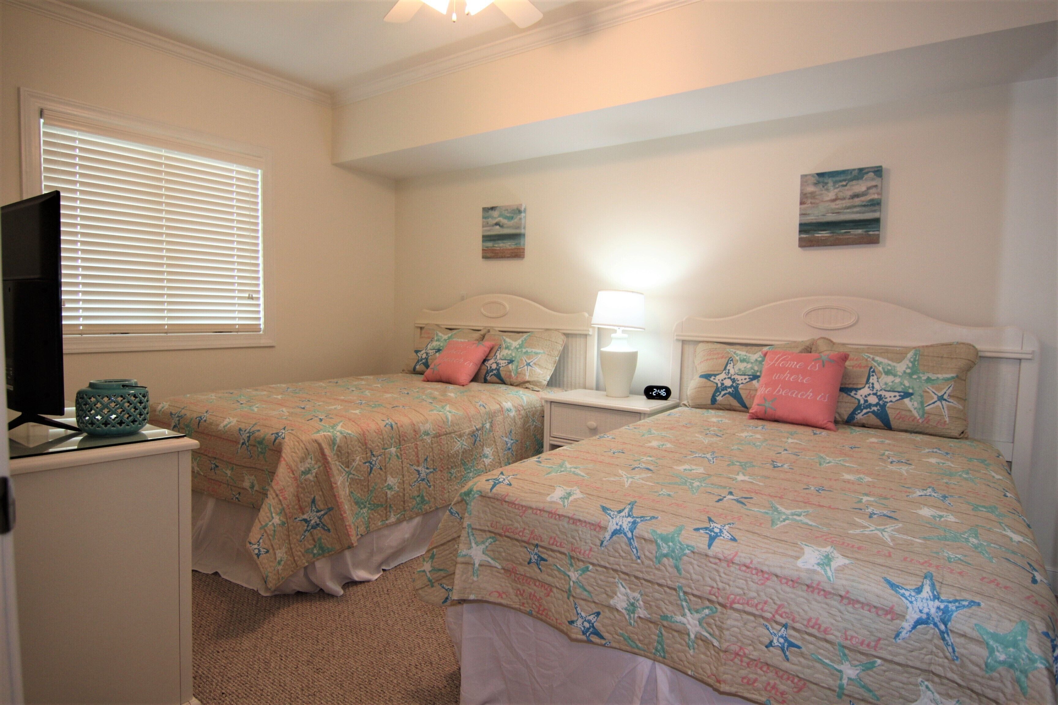 A bedroom with two beds, each with star-patterned bedding, a nightstand with a lamp, and a television on a stand.