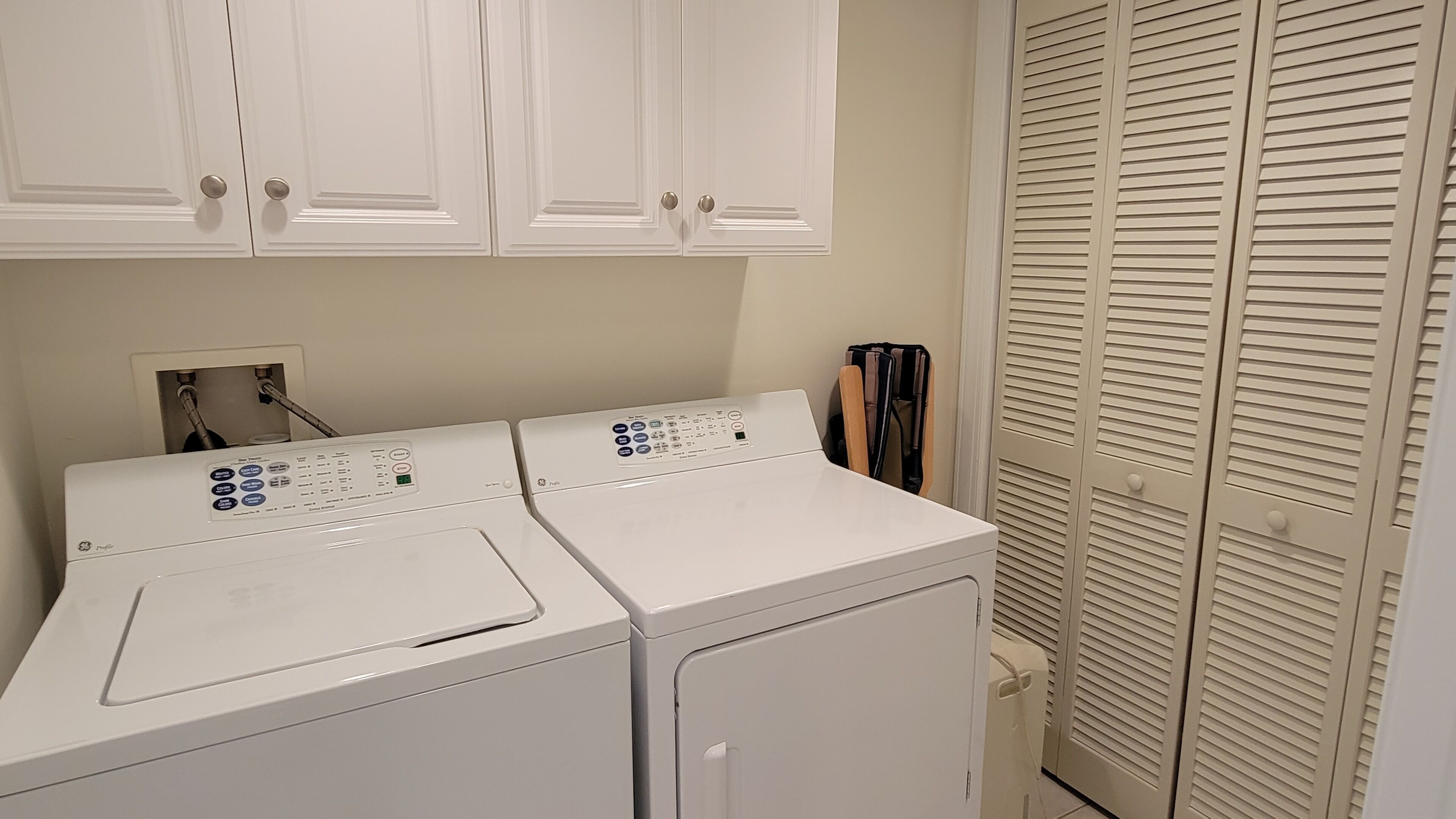 A laundry area with two front-loading washing machines, a utility sink, and a walk-in closet with louvered doors.