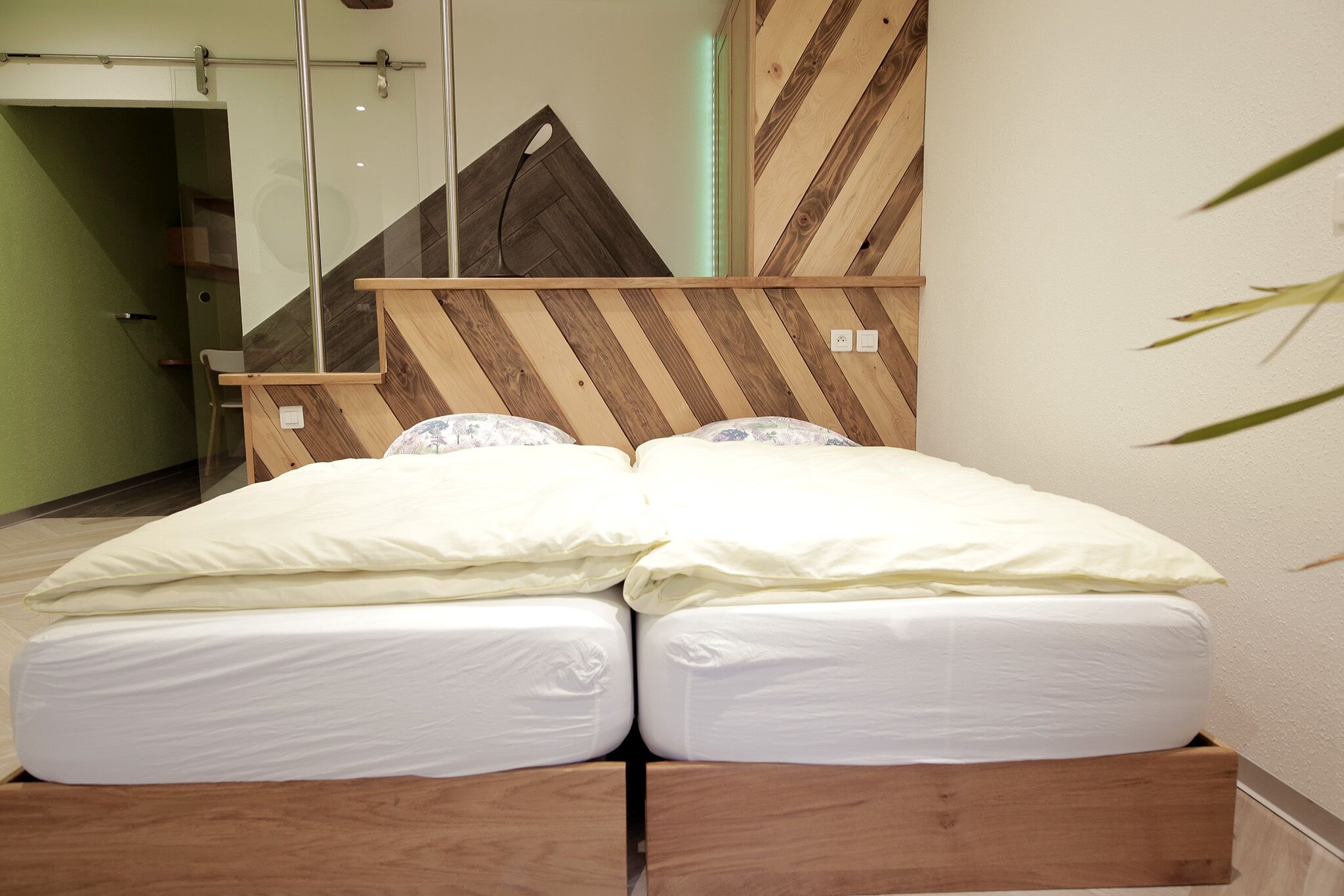A double bed with white bedding in a room with a wooden slatted headboard and a glass door leading to a staircase.