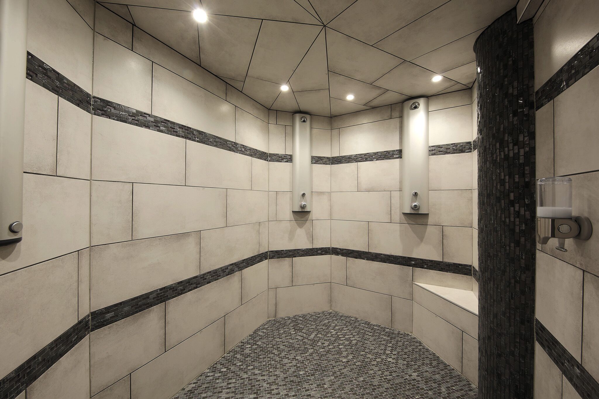 Zona de ducha en esquina con paredes de azulejos, suelo de mosaico blanco y negro y un secamanos.