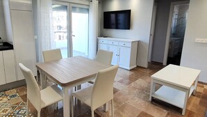 Una cocina moderna con armarios blancos, un televisor de pantalla plana y un comedor con una mesa y sillas de madera.