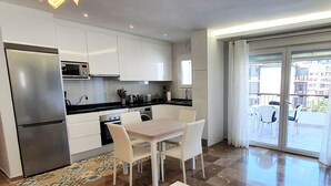 Una cocina moderna con armarios blancos, un refrigerador de acero inoxidable y un comedor con mesa y sillas blancas.