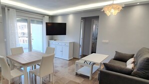 Una sala de estar moderna con comedor, televisor de pantalla plana en la pared y sofá gris.