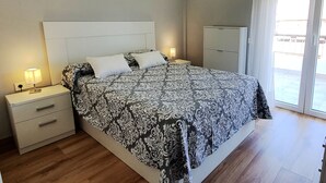 Un dormitorio con una cama grande, dos mesitas de noche con lámparas, un armario y un ventanal corredero al exterior.