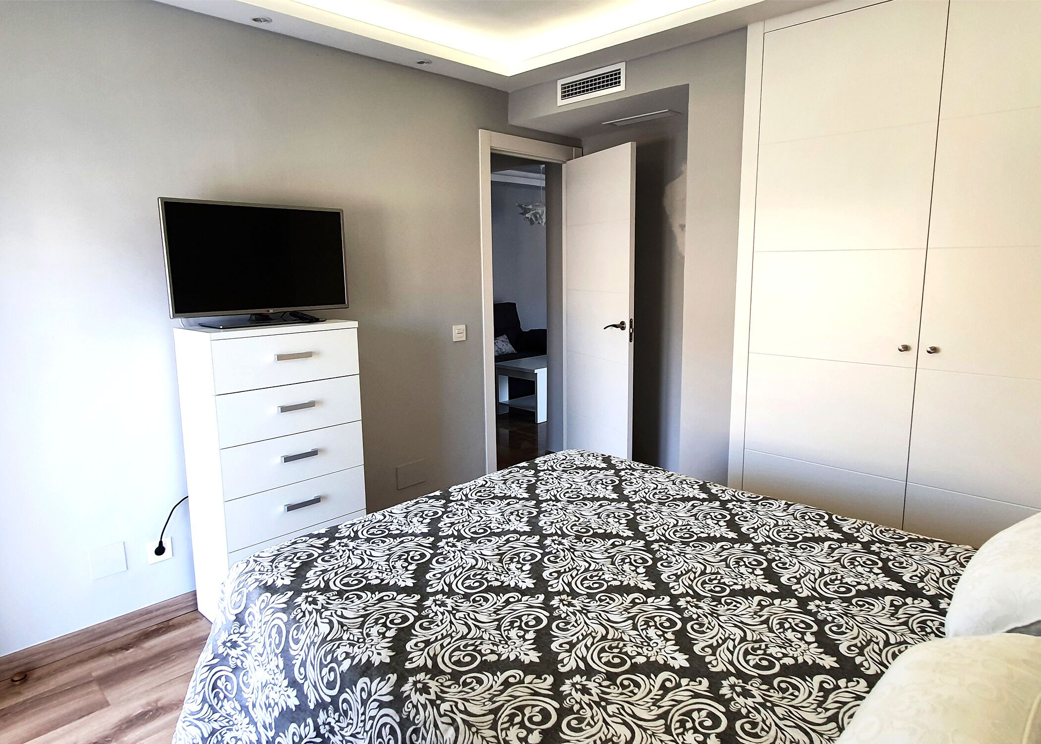 A bedroom with a bed, a TV on a dresser, a wardrobe, and a door leading to a bathroom.