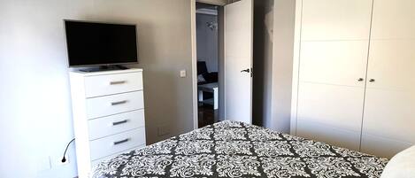 A bedroom with a bed, a TV on a dresser, a wardrobe, and a door leading to a bathroom.