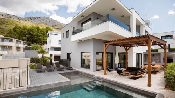 Una casa moderna de dos pisos con piscina, mobiliario exterior y una pérgola.