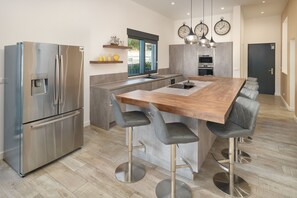 A modern kitchen with a stainless steel refrigerator, a wooden island with bar stools, and a built-in oven.