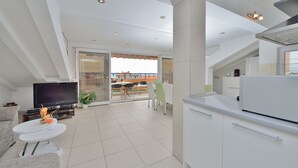 Una cocina moderna con armarios blancos, un comedor con una mesa redonda y un televisor en la sala de estar.
