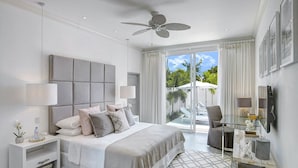 Un dormitorio moderno con una cama grande, mesitas de noche, un ventilador de techo y vistas al exterior.