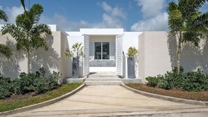 Un edificio moderno con fachada blanca, una entrada central con contraventanas abiertas y un camino de grava que conduce a la entrada.