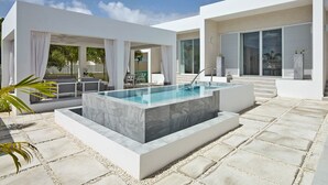 Un área de piscina moderna al aire libre con una piscina rectangular, paredes blancas y un deck con baldosas de piedra.
