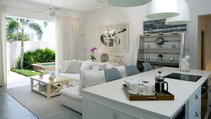 Een moderne woonkamer met een witte bank, salontafel en een keukeneiland met een dienblad vol ontbijtartikelen.