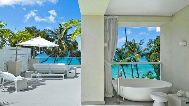Ein modernes Hotelzimmer mit Balkon, einer großen Badewanne und Blick auf einen tropischen Strand.