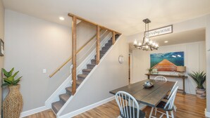 Un comedor con una escalera de madera, un candelabro y un cuadro en la pared.