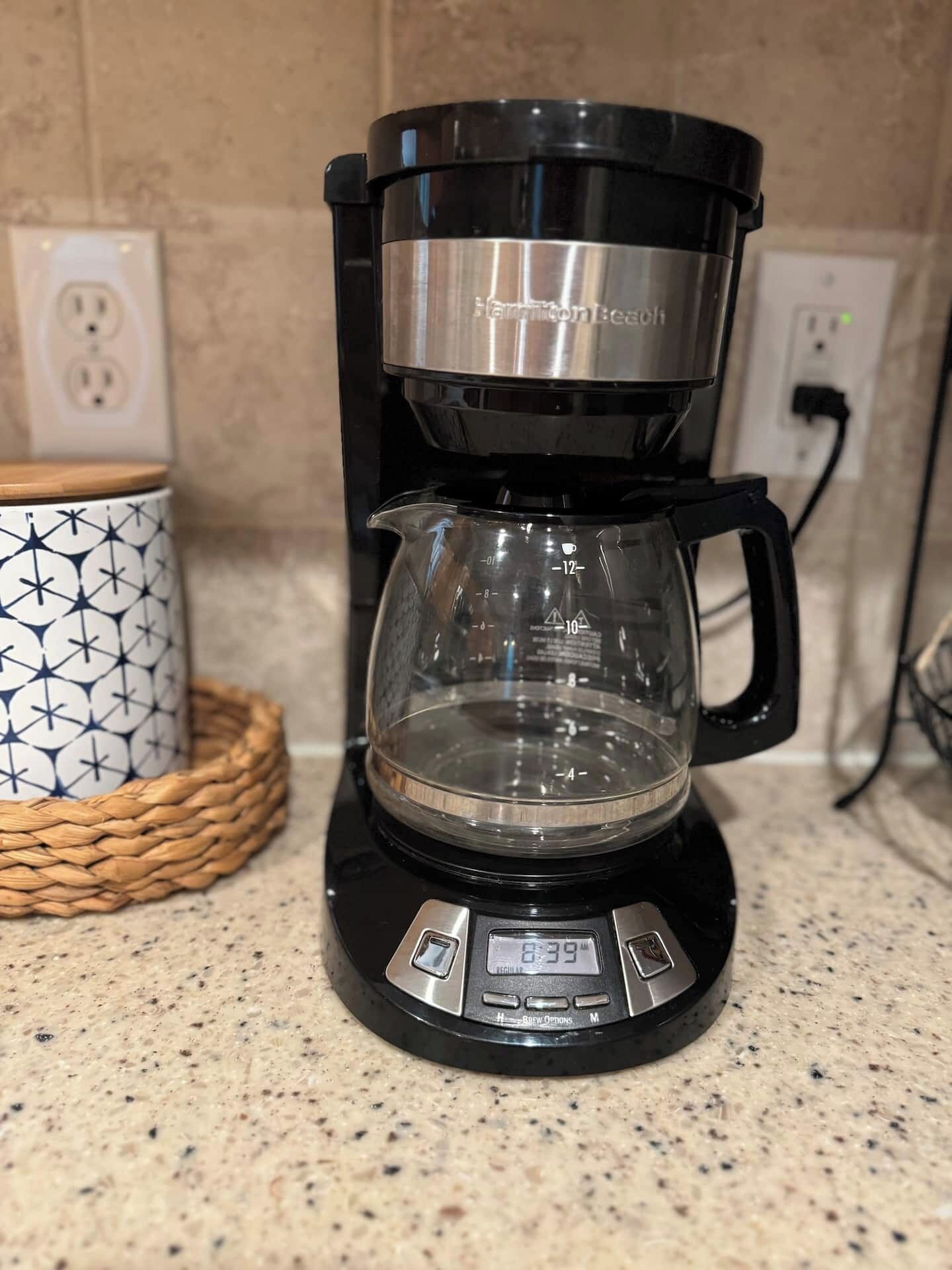A coffee maker with a digital display, a glass carafe, and a patterned mug on a kitchen counter.