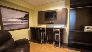 Una kitchenette compacta con televisión de pantalla plana, dos taburetes de bar y un microondas.