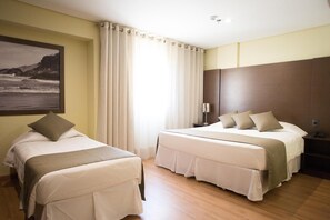 Habitación de hotel con dos camas, un ventanal con cortinas, un cuadro en la pared y suelo de madera.