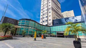 Un hotel moderno con fachada de vidrio curvada, zona de estacionamiento y palmeras.