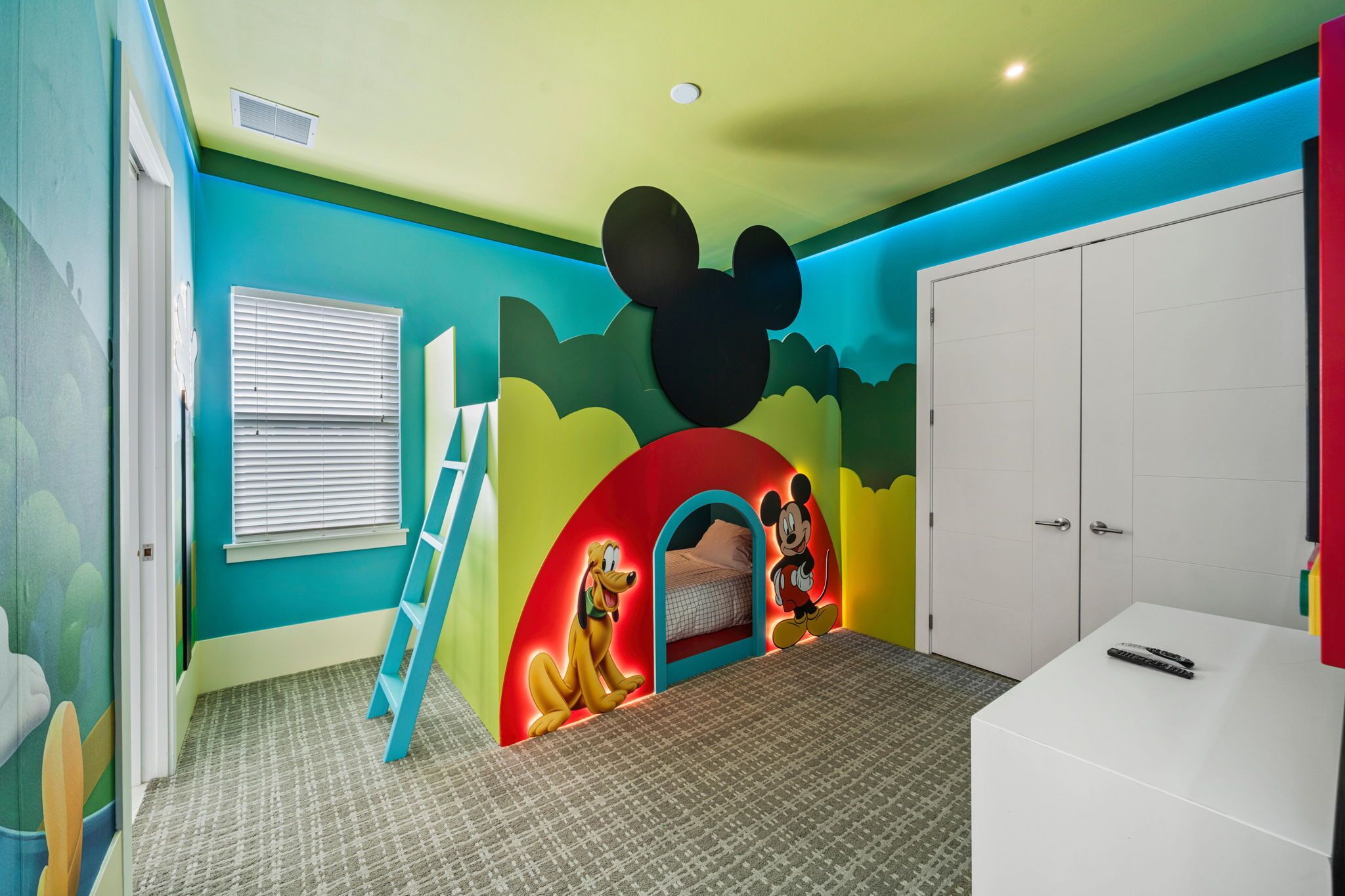 A child's bedroom with a Mickey Mouse mural, a bed, a wardrobe, and a small desk.