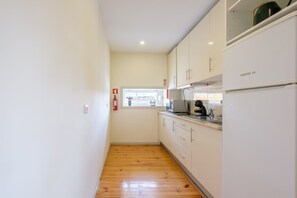 A narrow kitchen with wooden flooring, white cabinets, a microwave, and a refrigerator.