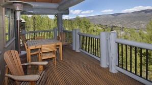 A wooden deck with a table and chairs, overlooking a mountainous landscape.