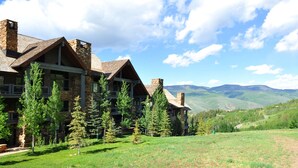A lodge with multiple buildings, surrounded by a grassy area and trees, with a mountainous backdrop.