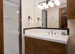 Un baño moderno con cabina de ducha de vidrio, un lavamanos blanco con dos grifos y armarios de madera.