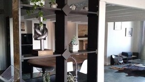 Et moderne interiør med en centralt placeret, sort reol, der viser diverse genstande, et spisebord og et siddeområde med en stol.