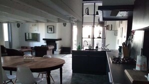 En moderne stue med et stort træspisebord, pejs og et køkkenområde med vask og bestik.
