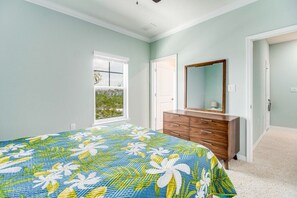 A bedroom with a floral bedspread, a wooden dresser, a mirror, and a window with a view. - Hale Piko, Lost Key Golf and Beach Resort NEW (Pensacola)