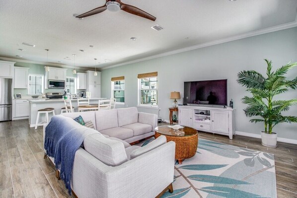 A spacious living room with a sofa, a coffee table, and a TV. There is a kitchen area with cabinets and a dining table. - Hale Piko, Lost Key Golf and Beach Resort NEW (Pensacola)