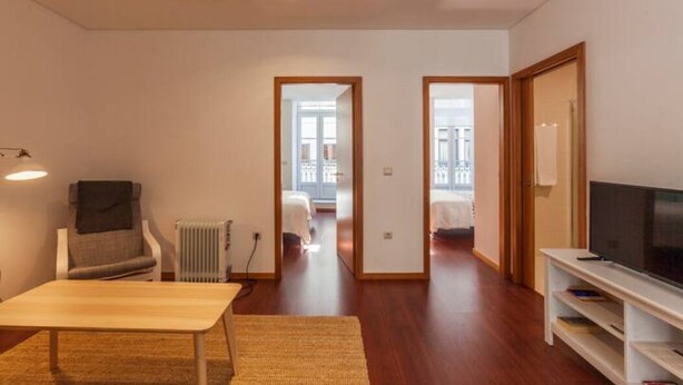 Una sala de estar moderna con sofá, una mesa de centro, televisor y radiador. Hay dos puertas que dan a otras habitaciones.