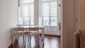 Una habitación con una mesa de comedor y sillas, ventanas amplias con vistas a un balcón y un sofá en la esquina.