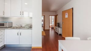 Una cocina moderna con armarios blancos, microondas y un lavamanos. Hay un comedor con una mesa y sillas.