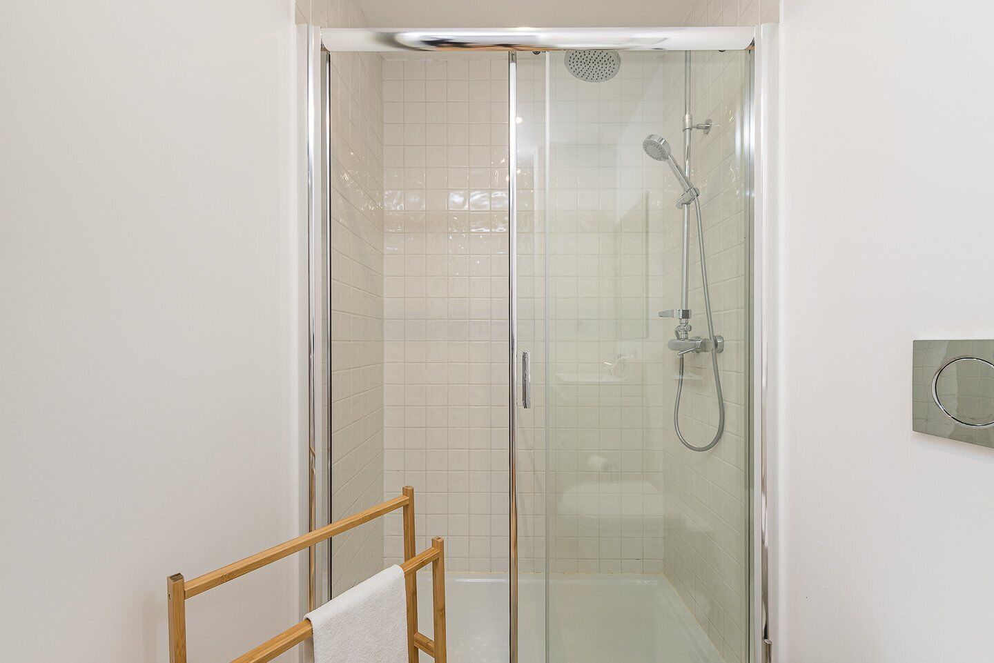A glass-enclosed shower with a handheld showerhead and a wall-mounted faucet.