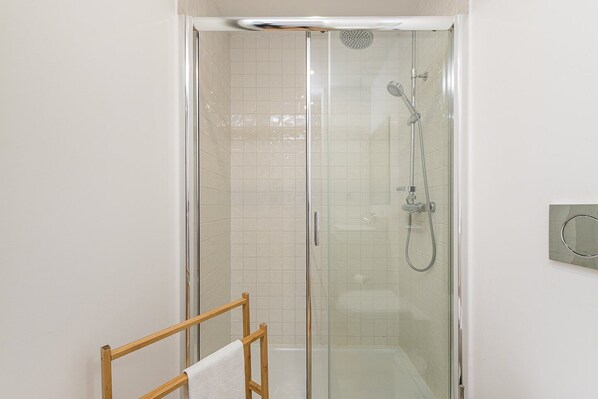 A glass-enclosed shower with a handheld showerhead and a wall-mounted faucet.
