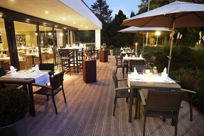 Un espace extérieur aménagé pour les repas, avec des tables et des chaises, un grand parasol et une vue sur le paysage environnant.