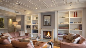 Een moderne woonkamer met leren banken, een glazen salontafel en boekenkasten. Een open haard is in het midden te zien.