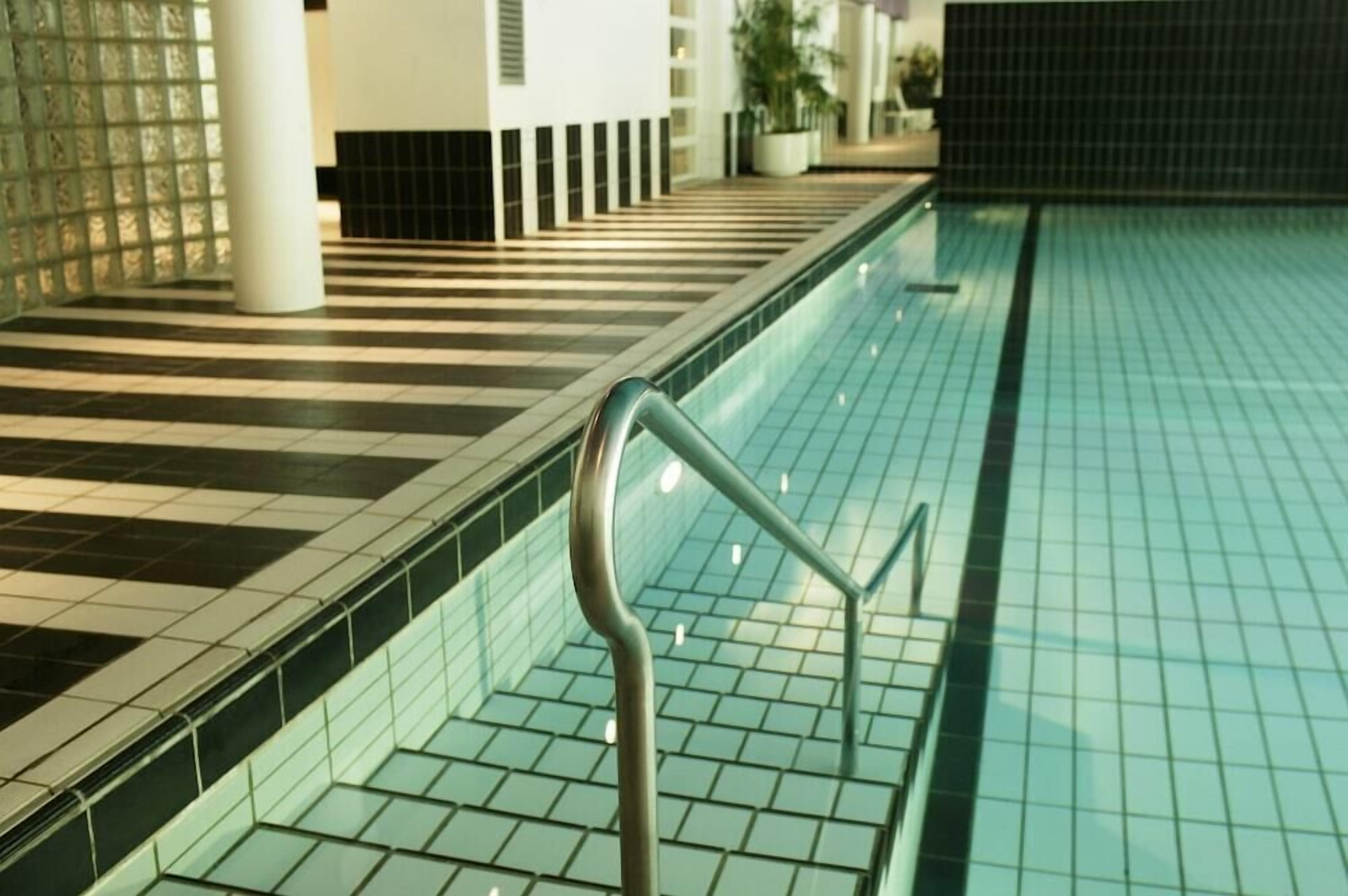 Piscina con suelo de azulejos y barandilla metálica.
